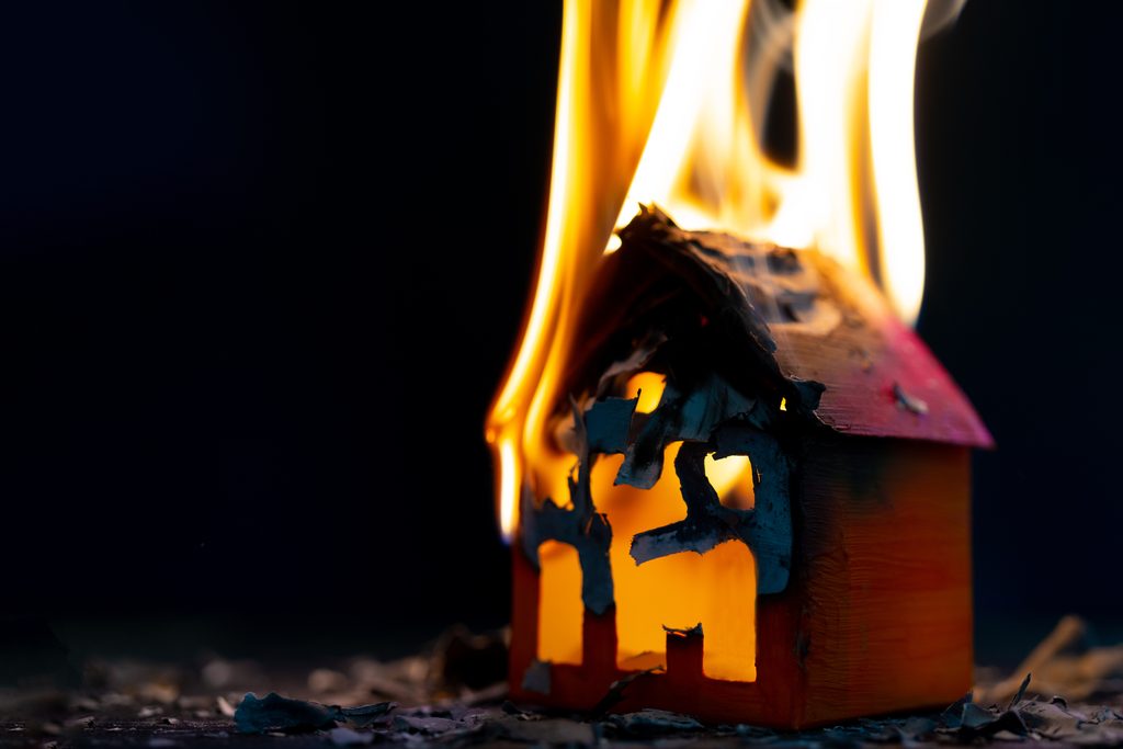 home fire insurance concept. miniature wooden residential house burns in fire.