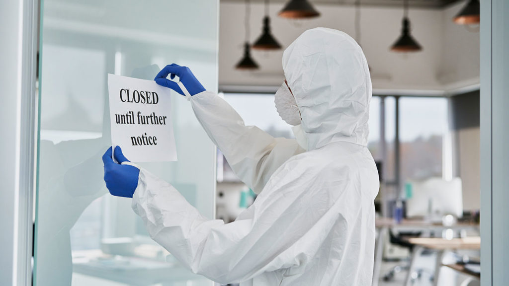 Photo of a sanitization professional hanging a closure sign on the door of a company experiencing business interruption due to COVID-19.