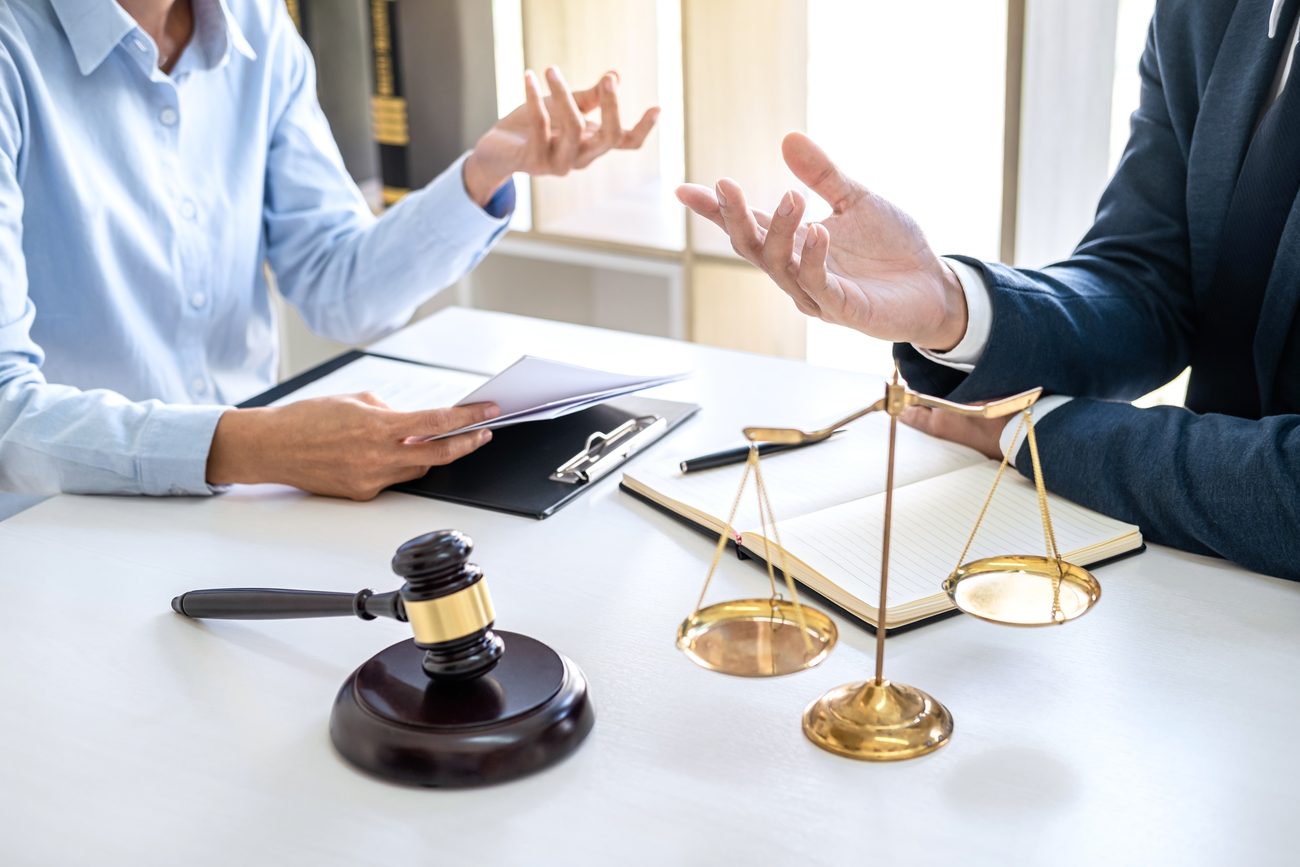 Two professionals in discussion at a legal desk with a gavel, scales of justice, and documents, symbolizing a legal or insurance consultation