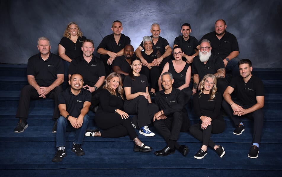 Portrait of the Avner Gat team wearing matching black company shirts, sitting on the stairs