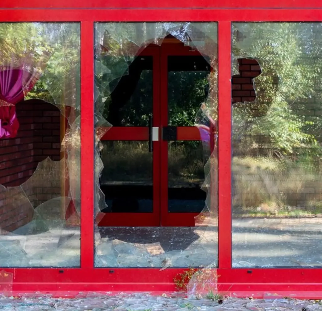 Close-up of a shattered glass window on a red frame, showing clear signs of residential property damage or vandalism for insurance claim documentation.